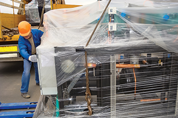 Technician installing a large chiller unit wrapped in protective plastic at an industrial facility