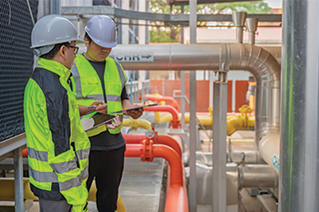 Two technicians inspecting chiller equipment and piping at an industrial HVAC facility
